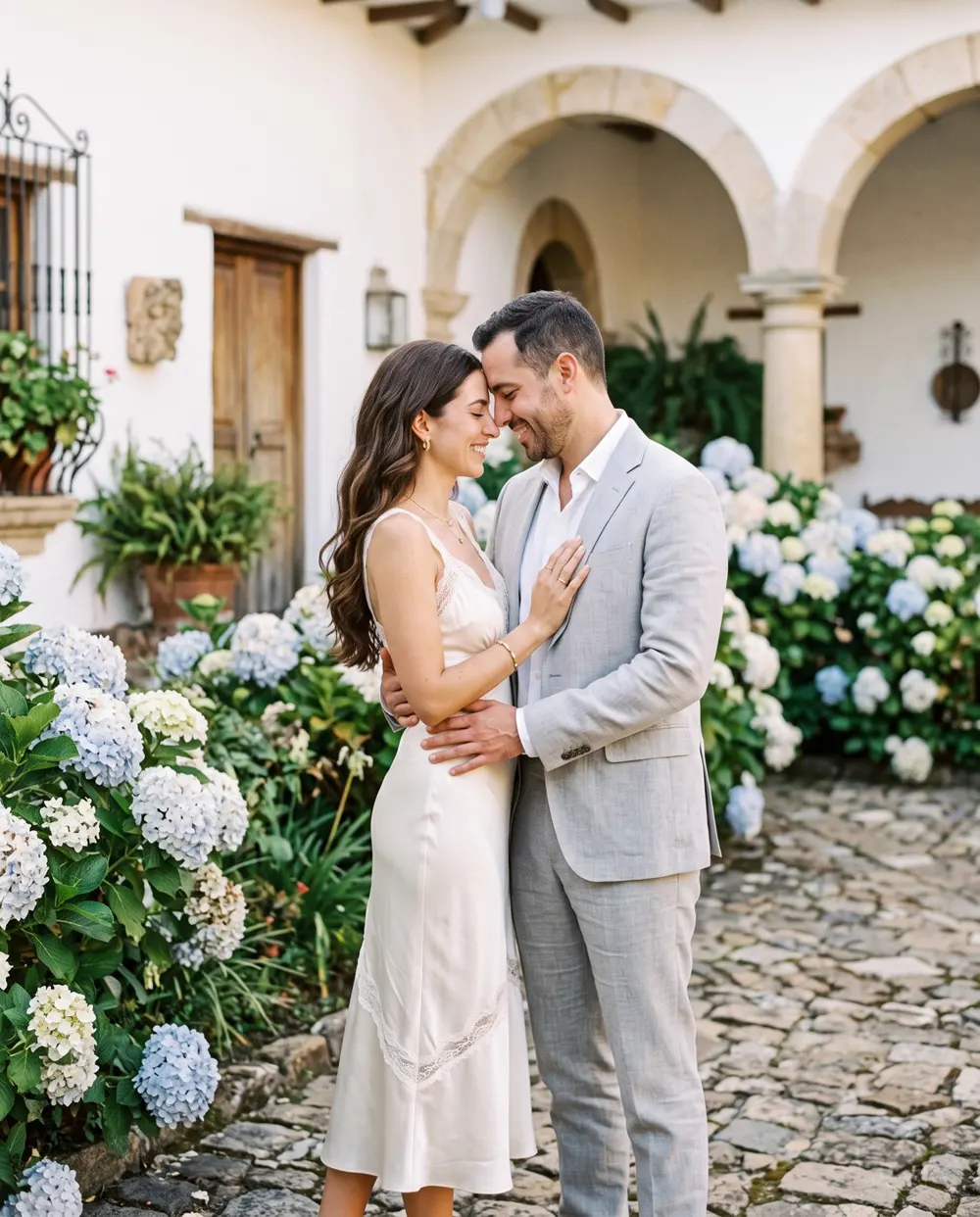 Una pareja abrazada en el patio de una hacienda con hortensias.